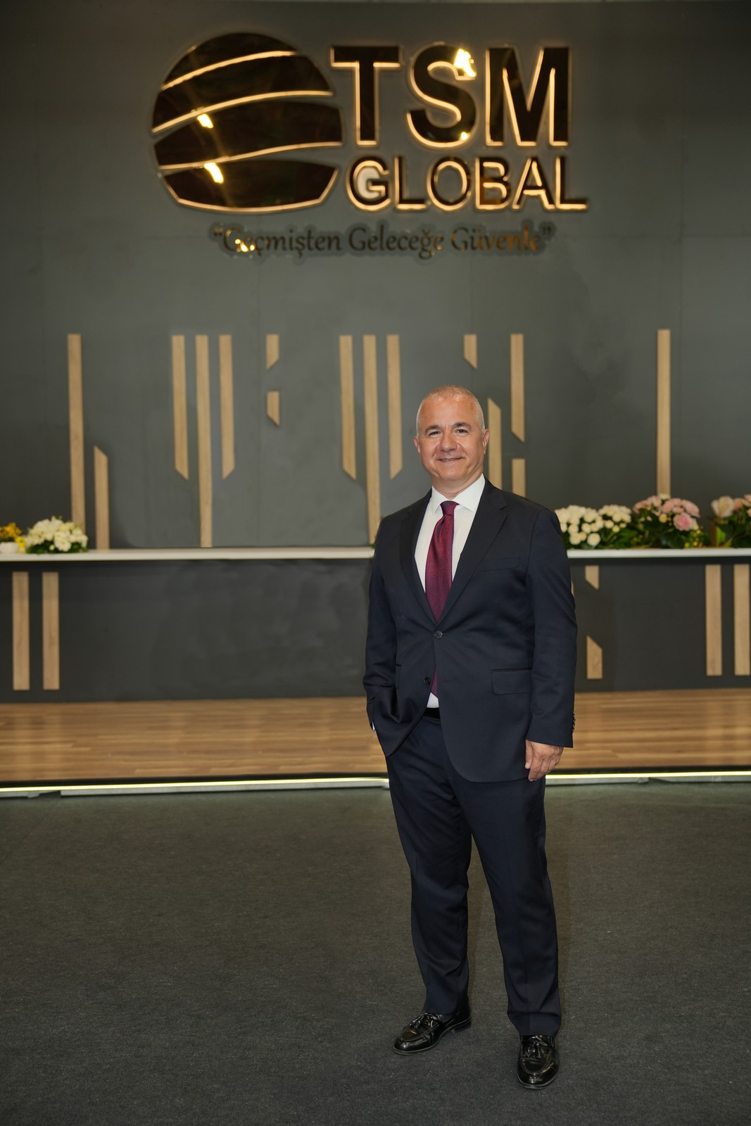TSM Global logosu önünde ayakta duran takım elbiseli temsilci.