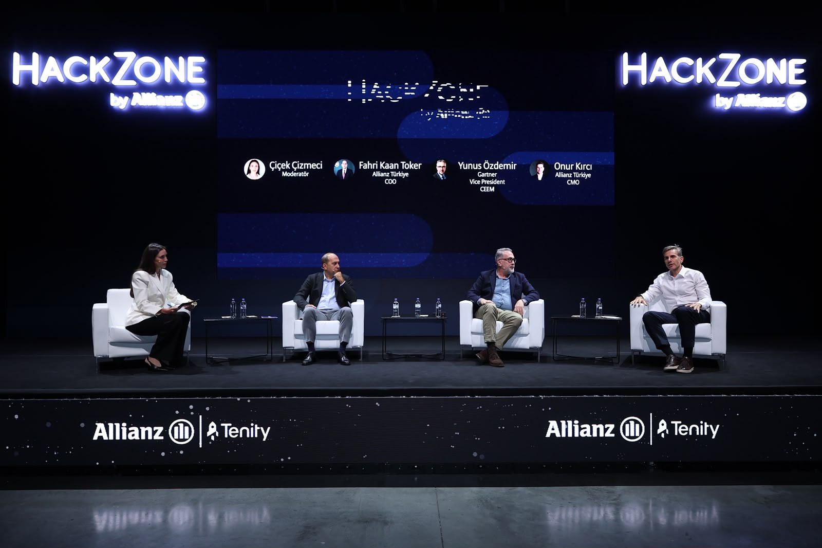 Sahnede beyaz koltuklarda oturan dört kişilik panel; arkalarındaki ekranda HackZone by Allianz görseli var.