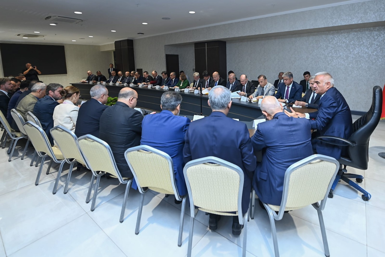 U biçimli masa çevresinde yetişkin yetkililer toplantı yapıyor.