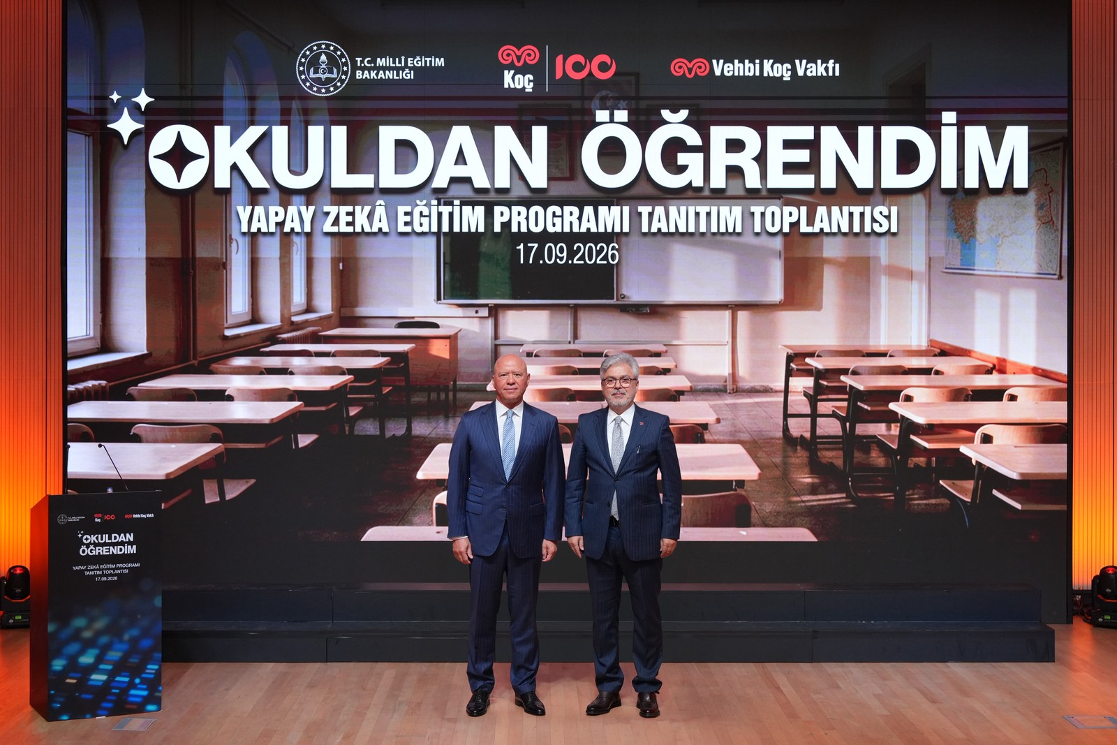 Yapay zekâ eğitim programı tanıtım sahnesinde iki yetişkin resmî temsilci.