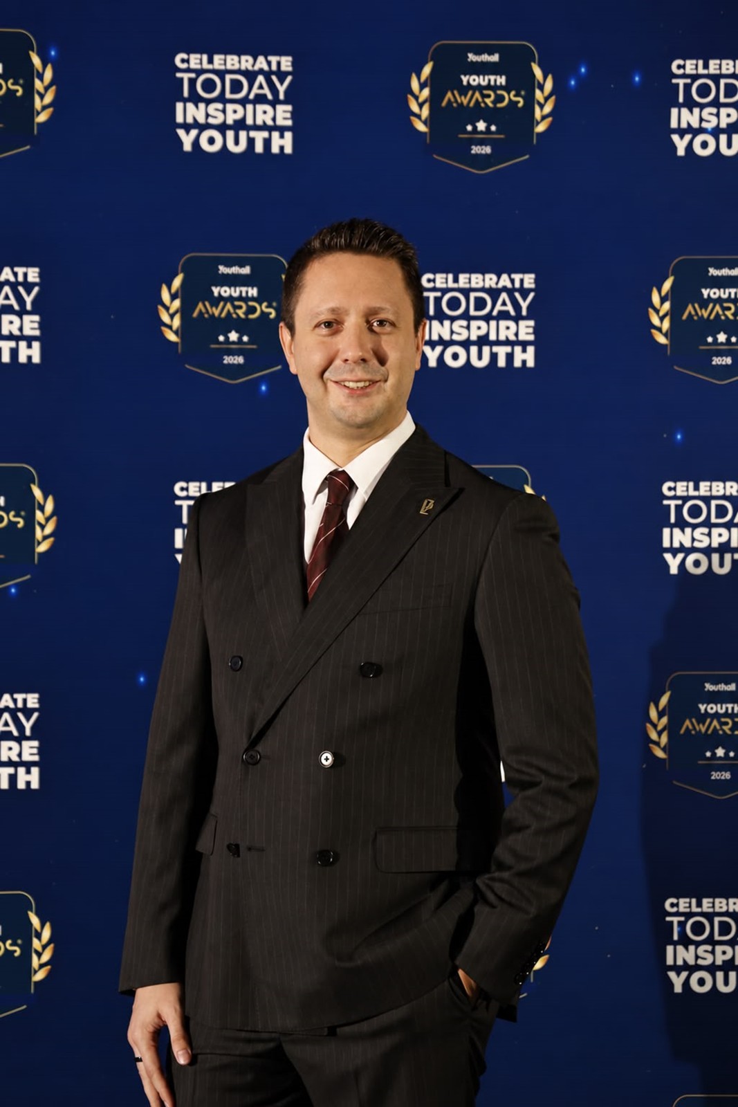 Youth Awards panosu önünde takım elbiseli yetişkin temsilci.