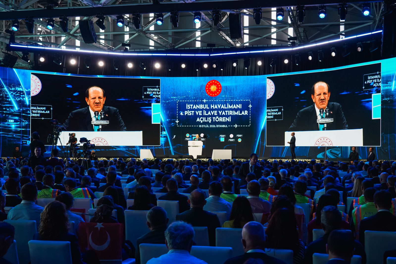 Havalimanı açılış salonunda konuşmacıyı ekranlardan izleyen davetliler.